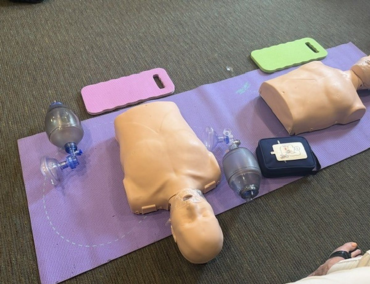 Manikins, bag valve masks and an AED trainer laid out on a training mat